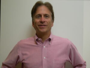 A man in pink shirt standing next to wall.